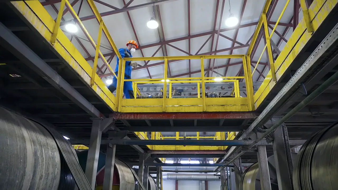 A worker on a yellow steel walkway above industrial plant equipment