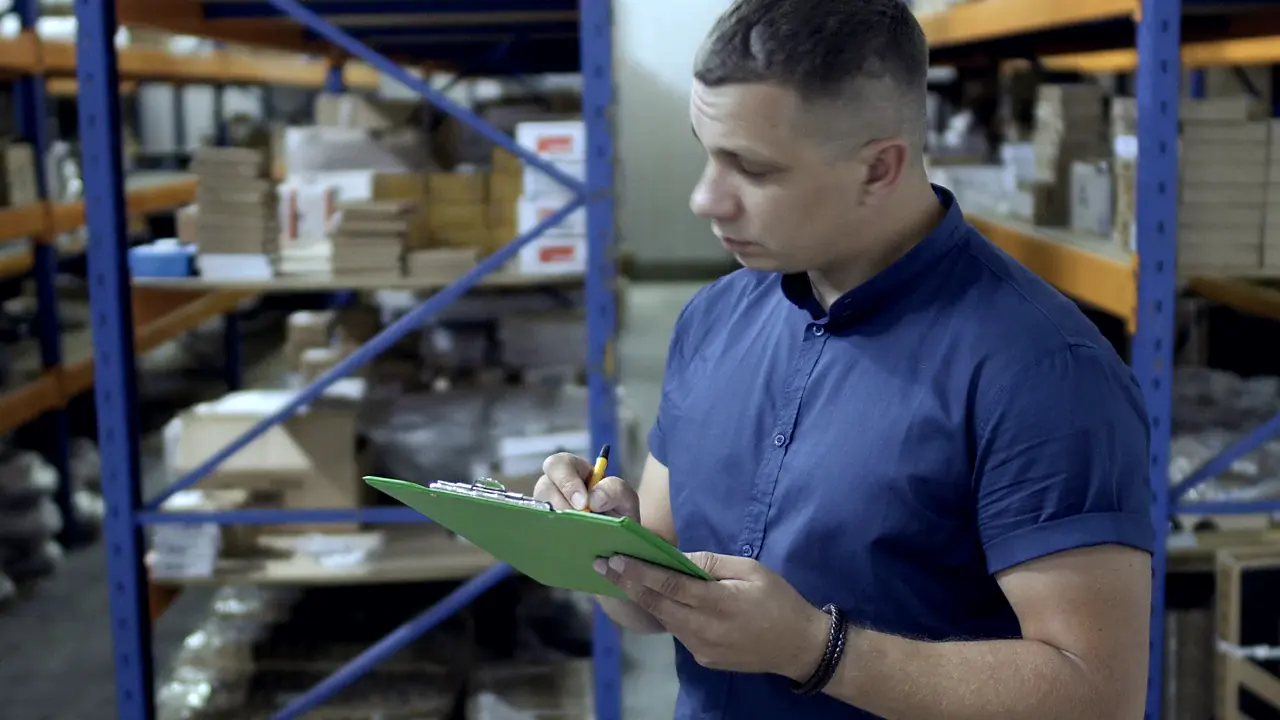 A man recording items on a clipboard between stocked warehouse racks