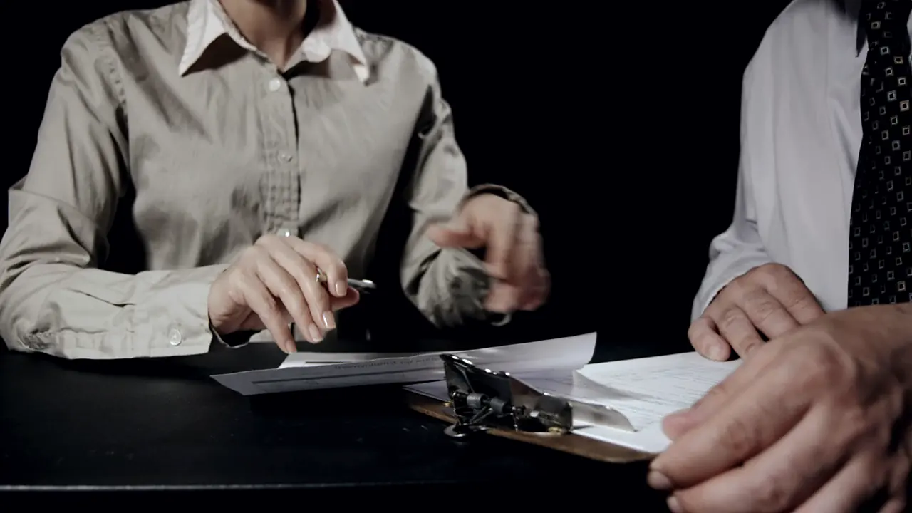 Two people reviewing printed reports on a clipboard at a desk